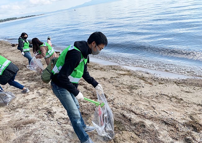 湖岸で参加者がトングを使い、砂浜のごみを拾っている様子