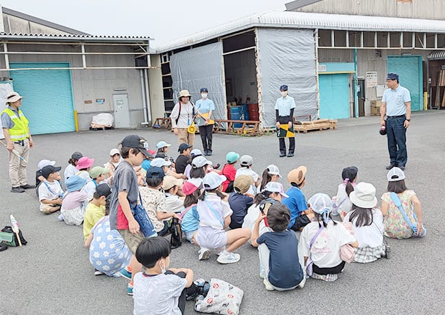 工場見学中、スタッフが児童たちに話しかけ、近距離で説明している様子。
