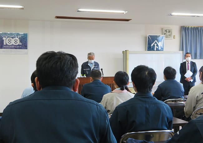 前方で登壇者が挨拶を行い、参加者が着席して聞いている会議の様子