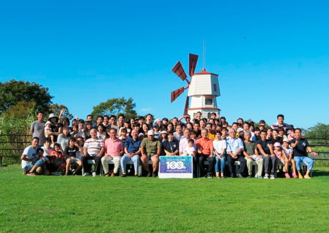 風車を背景に、社員と家族が集合して記念撮影をしている様子