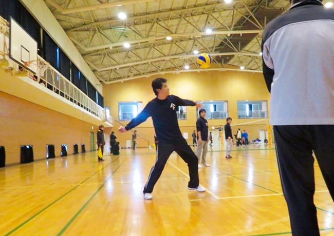 体育館でバレーボールのサーブを打つ参加者。ボールが宙に浮かぶ瞬間