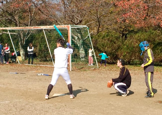 グラウンドでバットを構える参加者。キャッチャーと審判が構えている