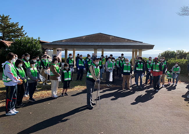 活動開始前に、緑のビブスを着た参加者たちが東屋前に集まり、説明を受けている様子