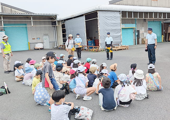 工場見学中、スタッフが児童たちに話しかけ、近距離で説明している様子。