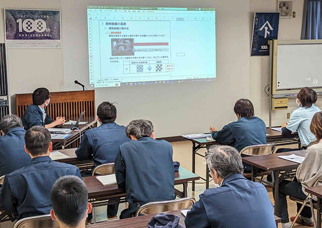 プロジェクターに資料を映しながら講師が説明し、参加者がメモを取っている研修の様子