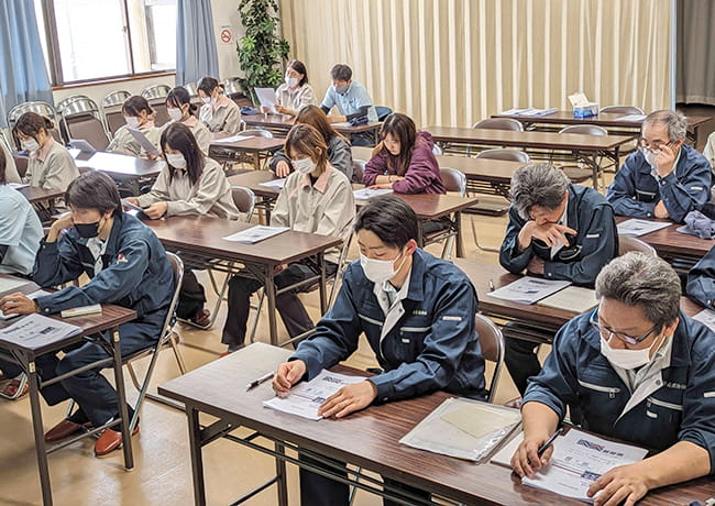 会議室で資料を見ながら真剣に講義を聞く社員たちの様子