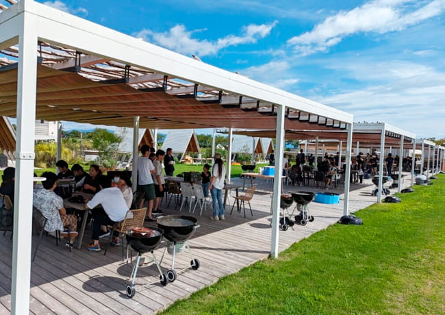 屋根付きテラスで社員や家族がバーベキューを楽しむ懇親会の様子