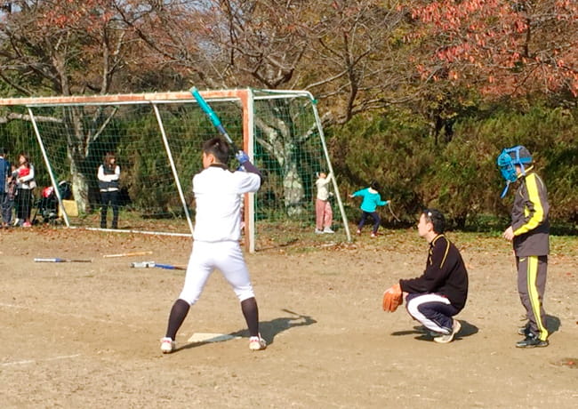 グラウンドでバットを構える参加者。キャッチャーと審判が構えている