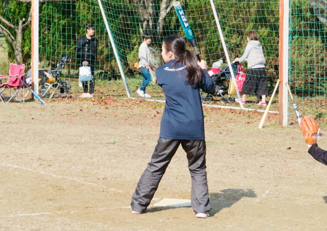 グラウンドでバットを構える女性参加者。後方では観客が見守っている